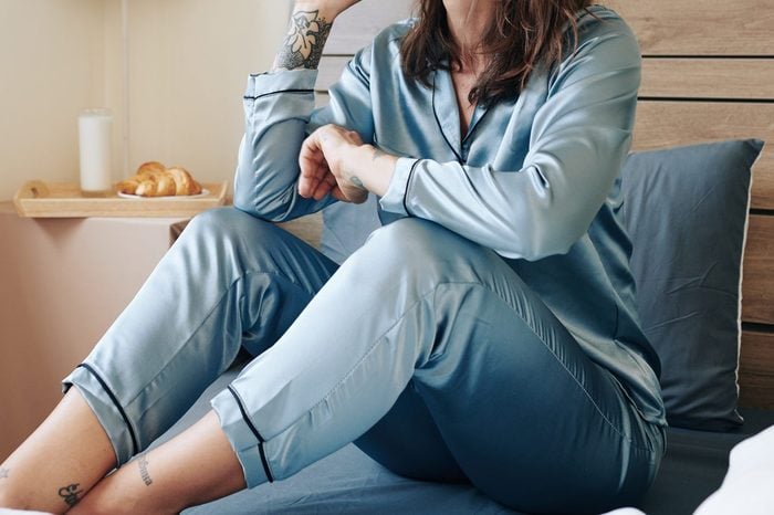 woman sitting on bed in blue silk pajamas