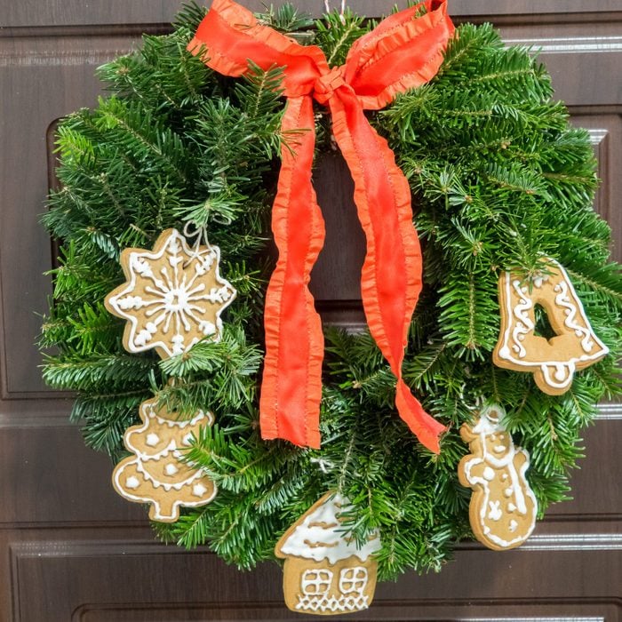 Christmas wreath decorated with handmade cookies and red ribbon hanging on the brown door.