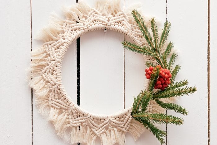 Creative Christmas wreath in the macrame style with fir branches and rowan berries is hanging on a white wooden wall