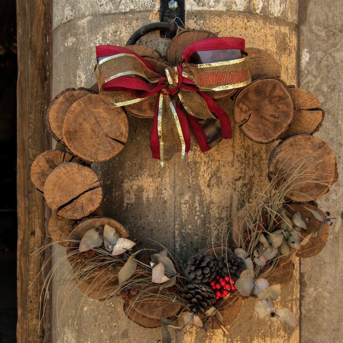 Rustic Christmas wreath decoration, made with with slices of wooden log, dried grasses and tree branches, pine cones and ribbon, hanging on a building exterior