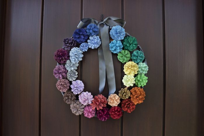 Multi-colored homemade decorative wreath made from painted pine cones, hanging on a wooden front door.