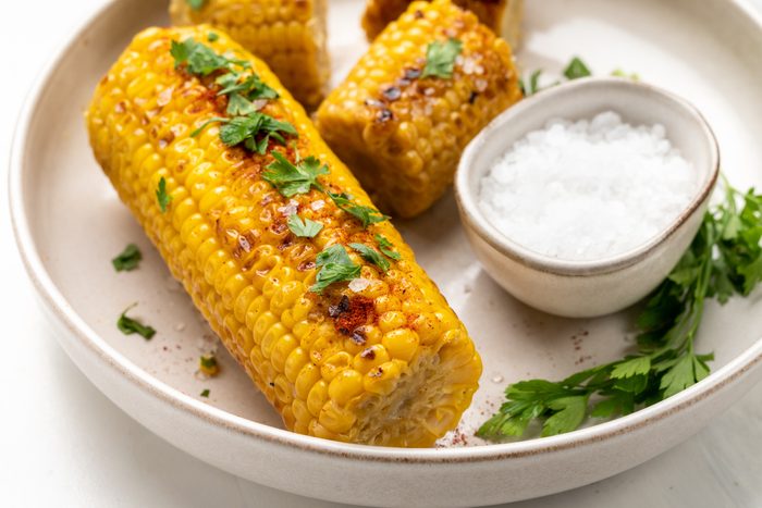 air fryer roasted corn with paprika salt and parsley on a white marble background