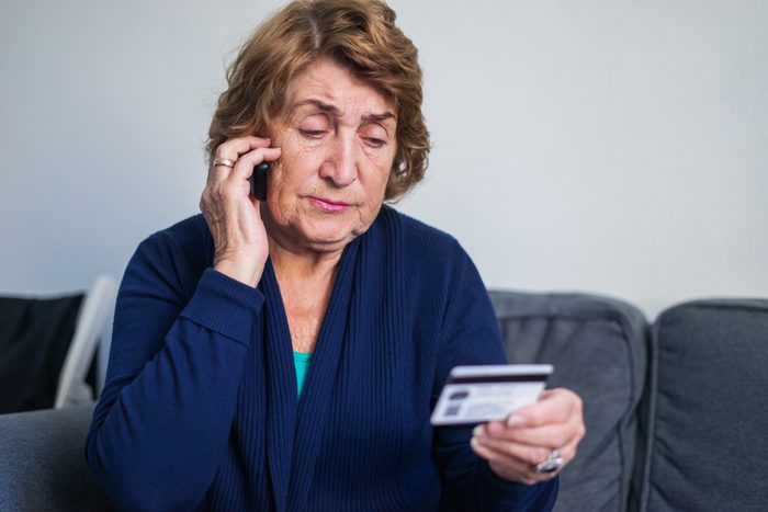 concerned senior woman using on the phone while holding credit card