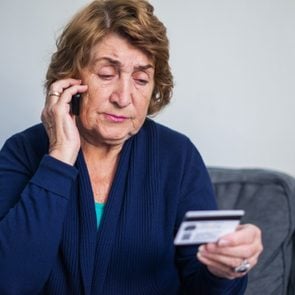 concerned senior woman using on the phone while holding credit card