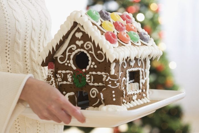 Woman holding gingerbread house on tray