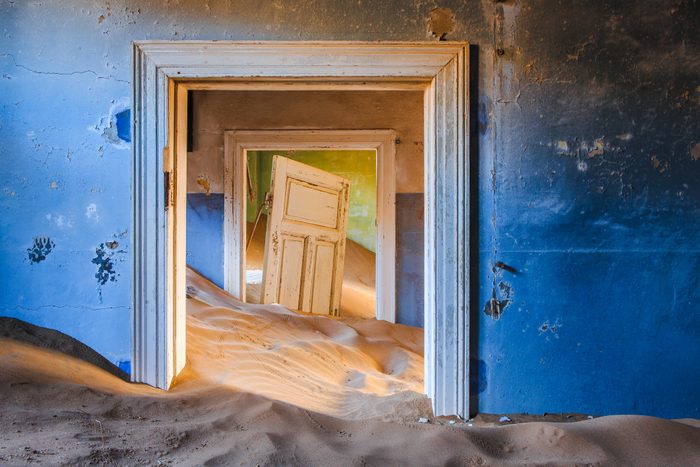 sand fills the interior of a building, seen through a series of doorways, in Kolmanskop Ghost town
