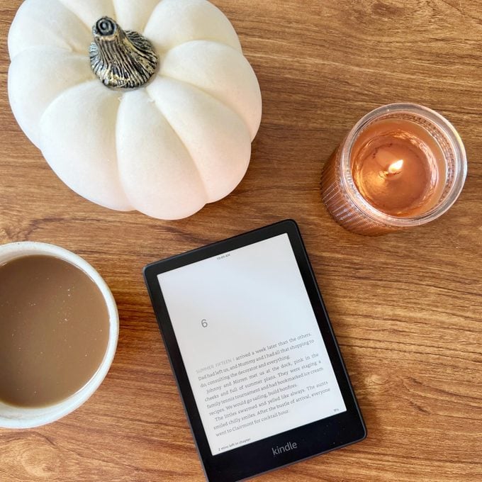 Kindle Paperwhite on a table with a candle, mini white pumpkin and a cup of coffee, viewed from above