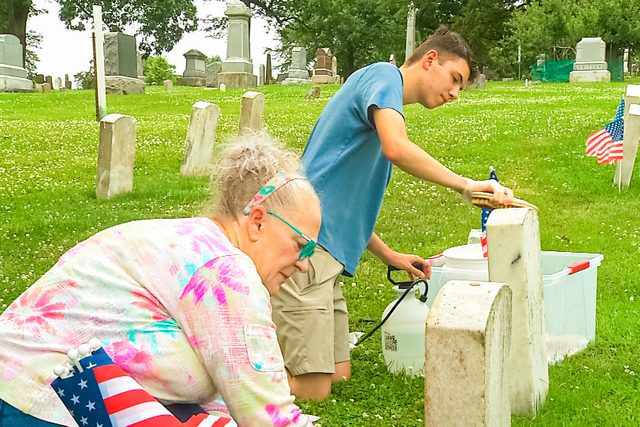 Madonna White and Aaron Schultz plant American flags near each cleaned headstone.