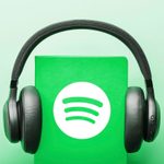 headphones on a green book with spotify logo. green background. audiobook concept