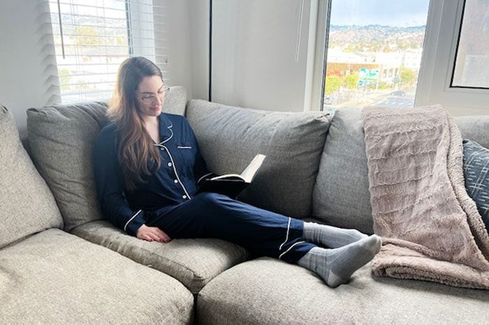Reina sitting on the couch reading while wearing Cozy Earth Bamboo Pajamas