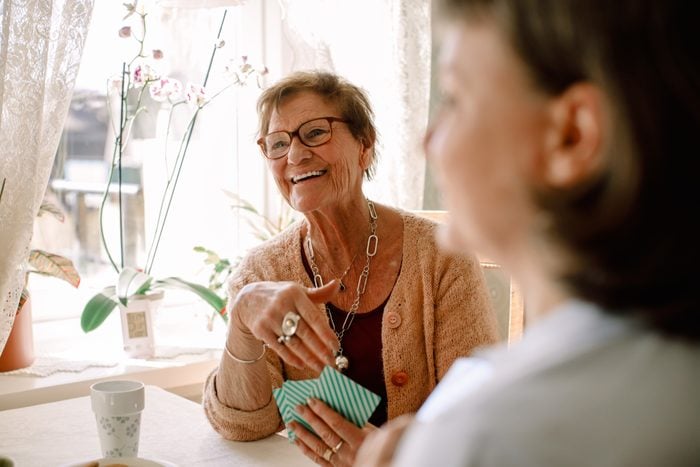 Smiling retired senior woman looking away while playing cards with social worker at nursing home