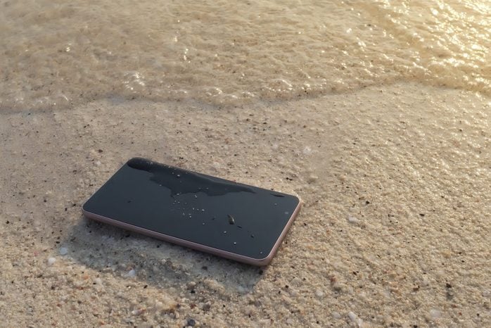 Mobile smart phone on the sandy beach with soft waves of sea background. Internet of things concept.