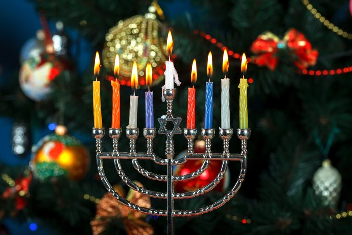 Close-Up Of Illuminated hanukkah Candles in a menorah And Christmas Decorations in the background