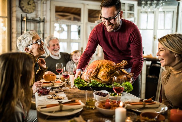 Young happy man serving Thanksgiving turkey for his family at dining table.