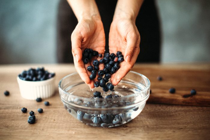 hands scooping blueberries out of a vinegar wash bowl