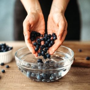 hands scooping blueberries out of a vinegar wash bowl