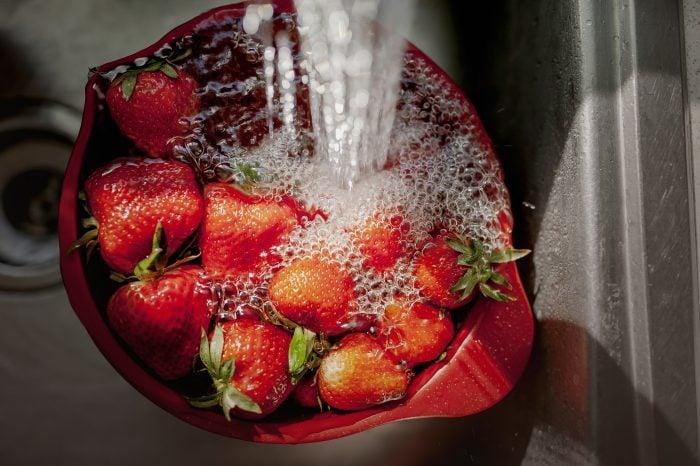 Bowl of Strawberries Under Running Water in a Kitchen Sink