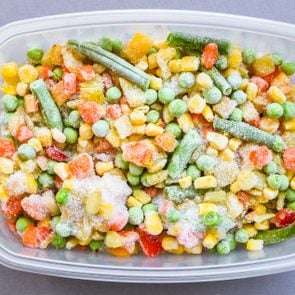 Frozen mixed vegetables with freezer burn in a plastic container on gray counter background