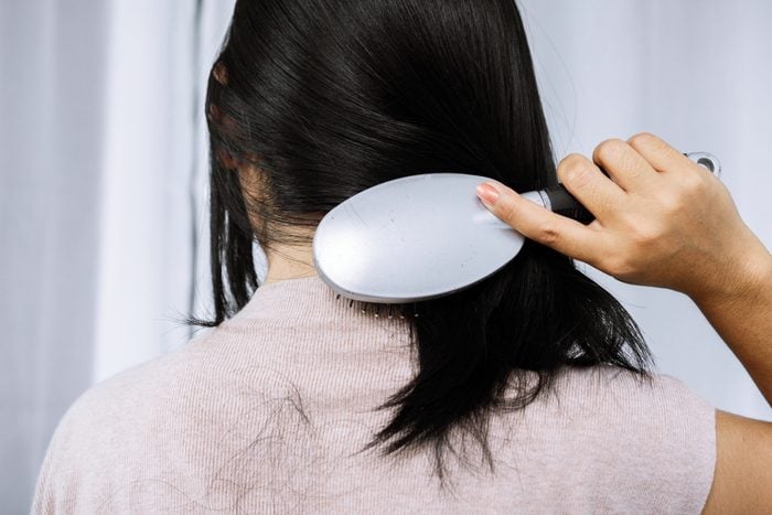 woman holding comb brushing her hair having problem with hair loss falling on back