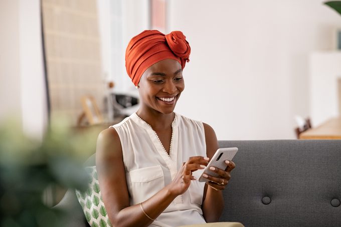 Smiling black woman with african turban using smartphone at home