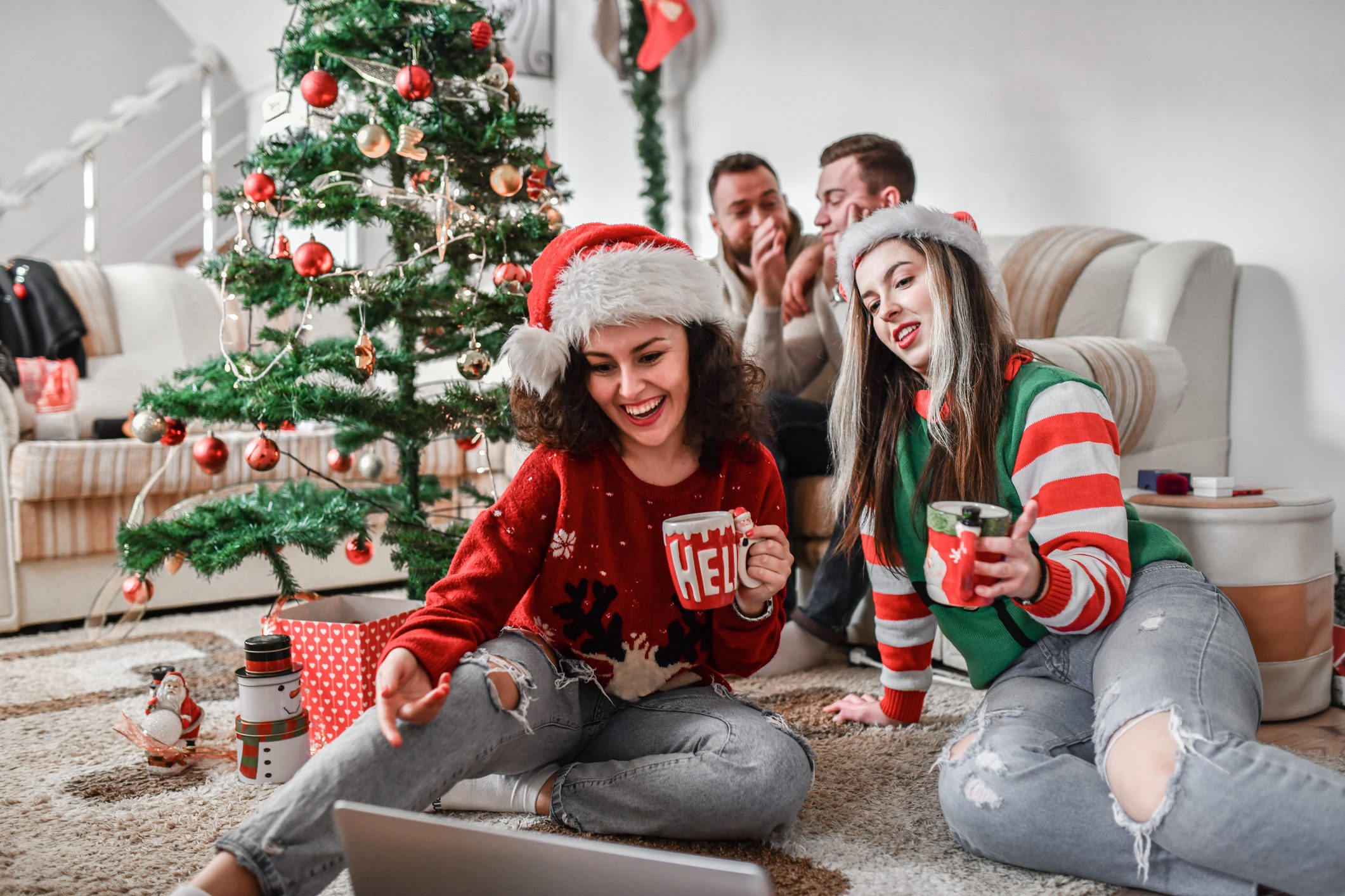 Smiling Females Enjoying TV Show On Laptop And Annoying Boyfriends During Christmas Party