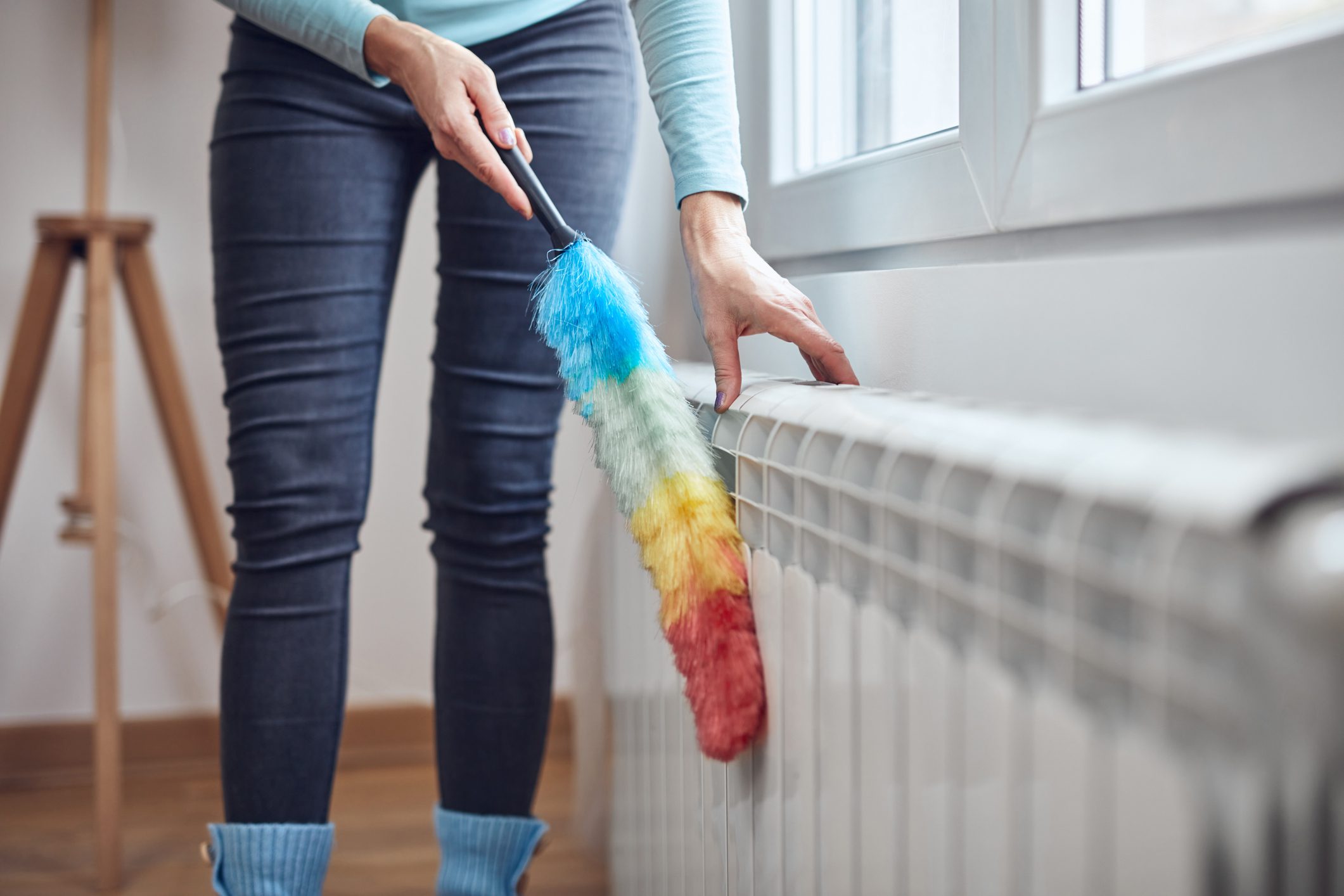 Woman with a dust stick cleaning central heating gas radiator at home.