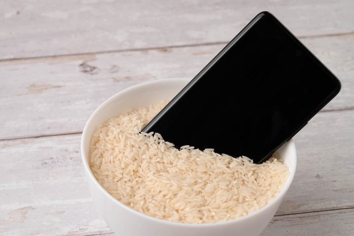 A mobile phone placed to dry in a bowl full of rice after the phone fell into water. Light wooden table background.