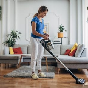 Woman vacuuming the living room with cordless vacuum cleaner
