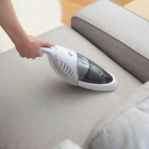 Woman with handheld vacuum cleaning on sofa