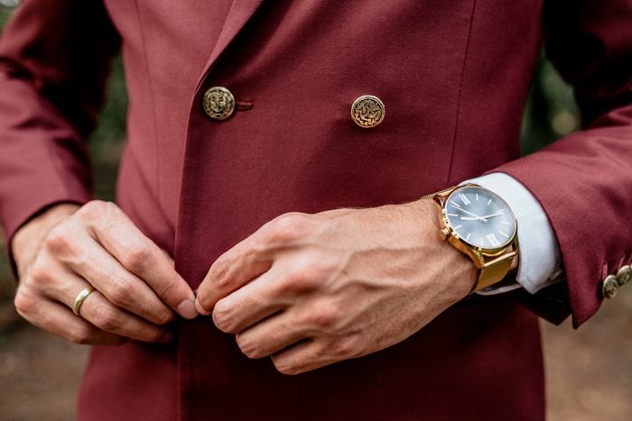 Close-up of man wearing a suit and golden watch buttoning his jacket