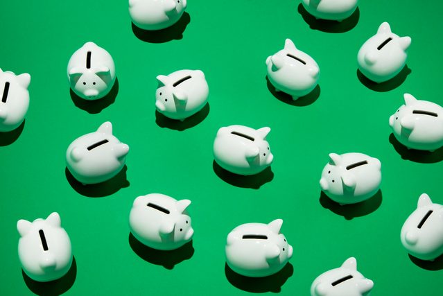 16 small white piggy banks placed randomly on green surface, high angle of view