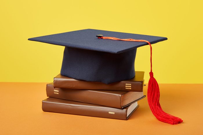 Academic cap and brown books on orange surface with yellow background