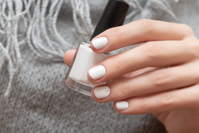 Female hand with white nail design holding nail polish bottle.