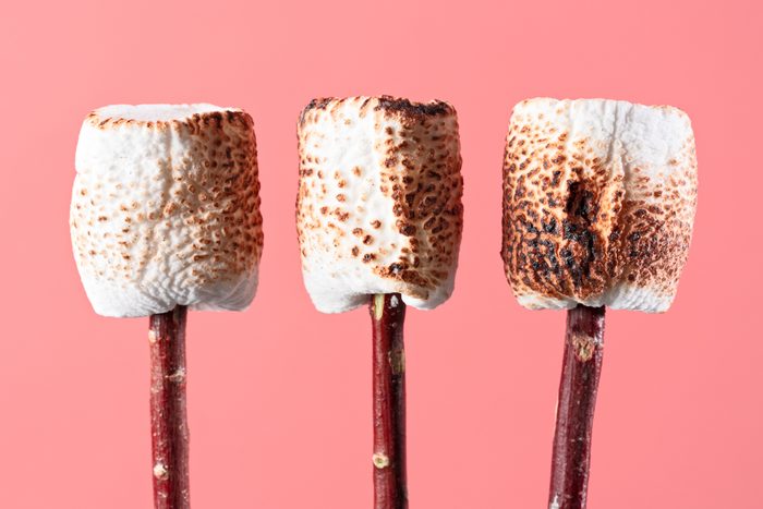 three Roasted Marshmallows on Twigs on a pink background