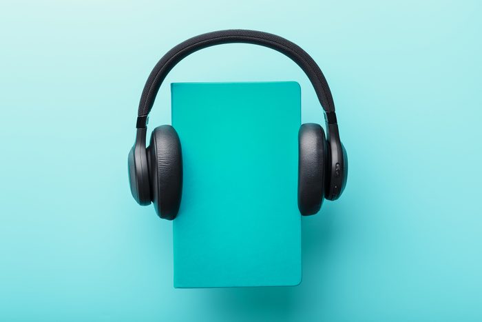 Headphones are worn on a book in a blue hardcover on a blue background, top view, audiobook concept