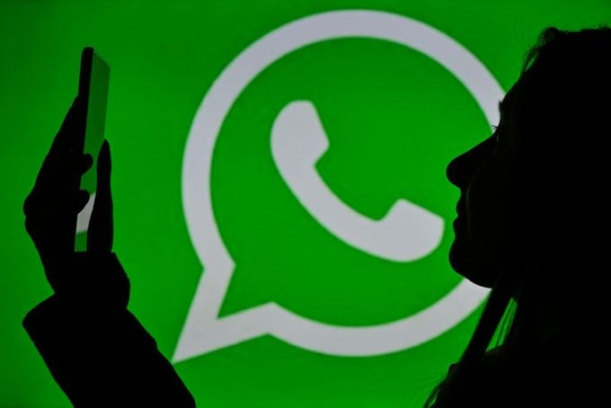 silhouette of a person holding a cell phone in front of a WhatsApp Messenger logo displayed on green background.