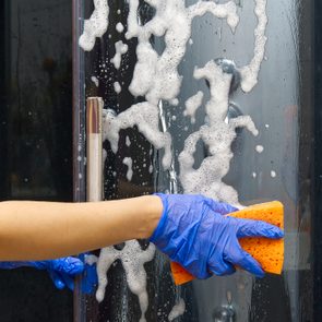 Cleaning of shower steam cabins from calcium deposits. Cleaning in the bathroom. hand in gloves with rag and detergent washing shower and glass