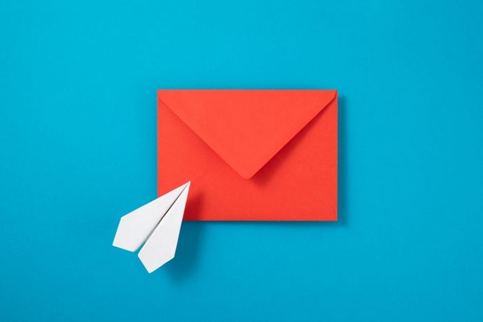red greeting card envelope and small paper airplane on blue background
