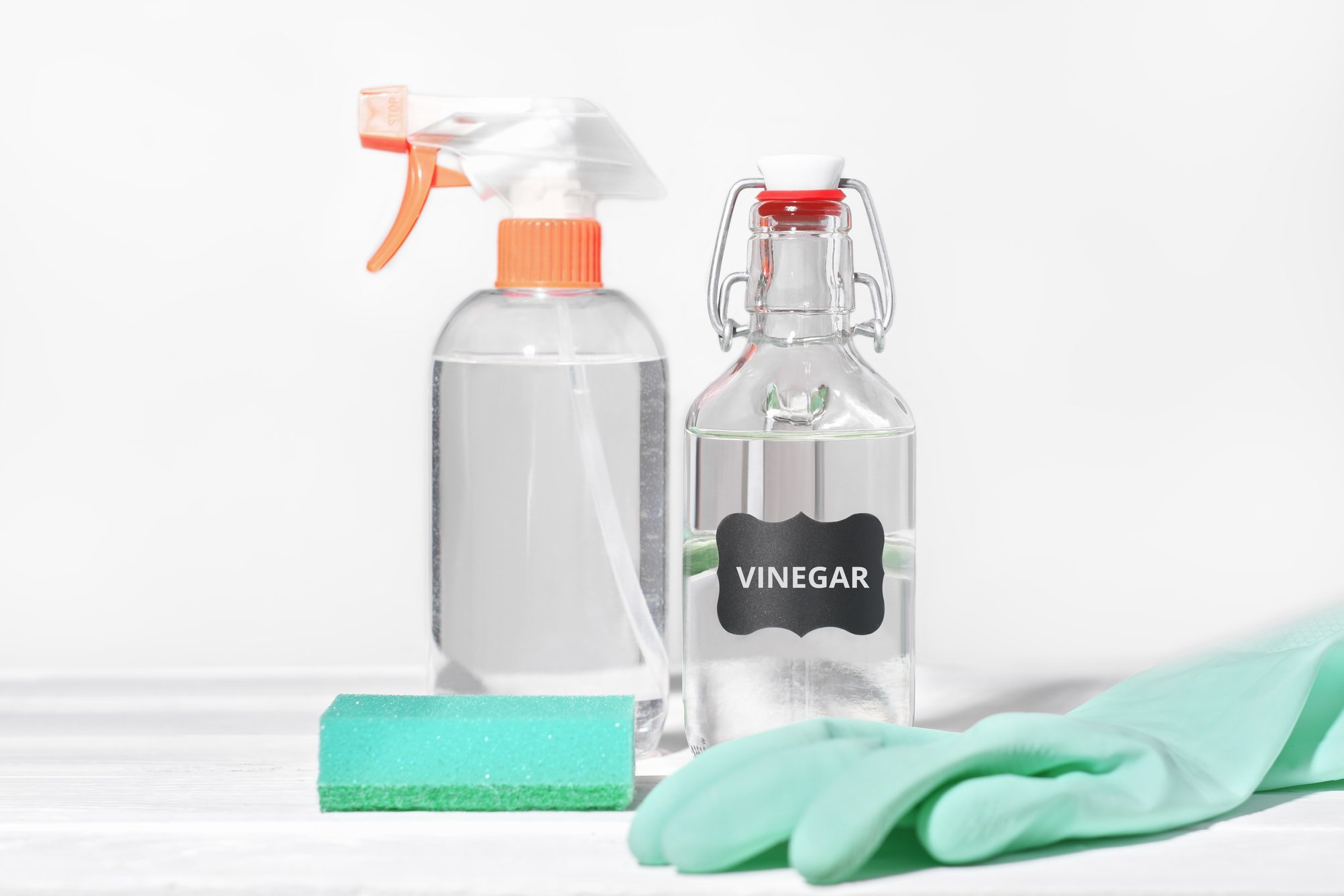 Housework white vinegar, natural household detergent, inexpensive cleaning product, rubber glove and kitchen sponge next to spray bottle.