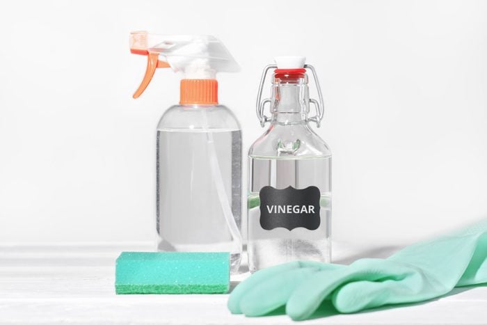white vinegar for home cleaning chores, natural householding detergent, affordable product for housekeeping, rubber glove and kitchen sponge next to sprayer bottle.
