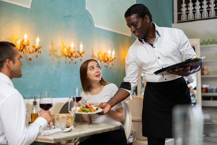 African american waiter bringing ordered dishes to couple at restaurant