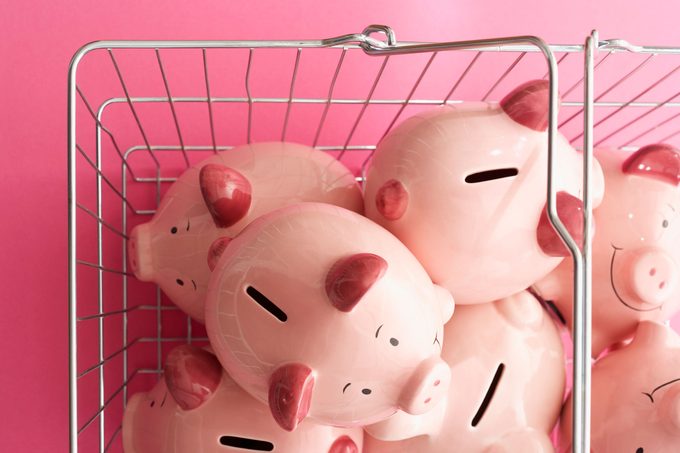 overhead view of metal grocery shopping basket filled with pink piggy banks on pink background