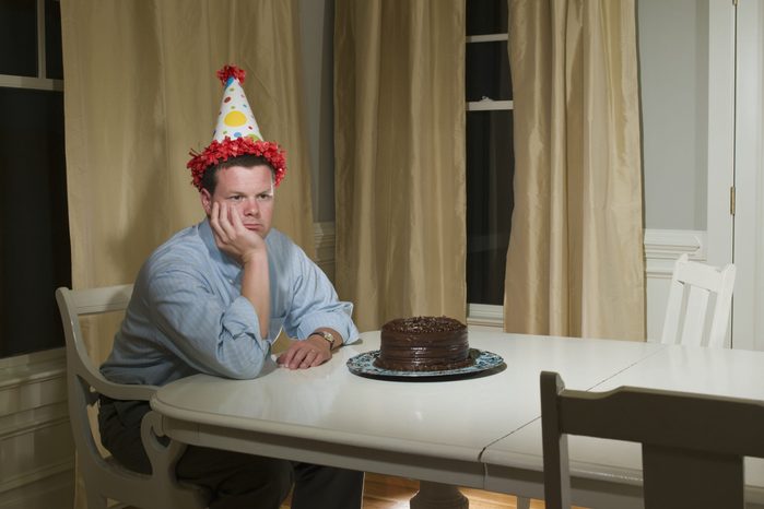 Mid adult man in party hat, sitting at table in front of birthday cake