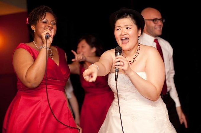 a woman singing karaoke at her wedding with another woman singing with her in a pink dress