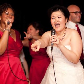 a woman singing karaoke at her wedding with another woman singing with her in a pink dress