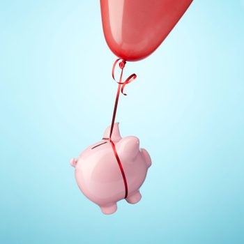Piggy Bank Tied To red Balloon floating against blue background