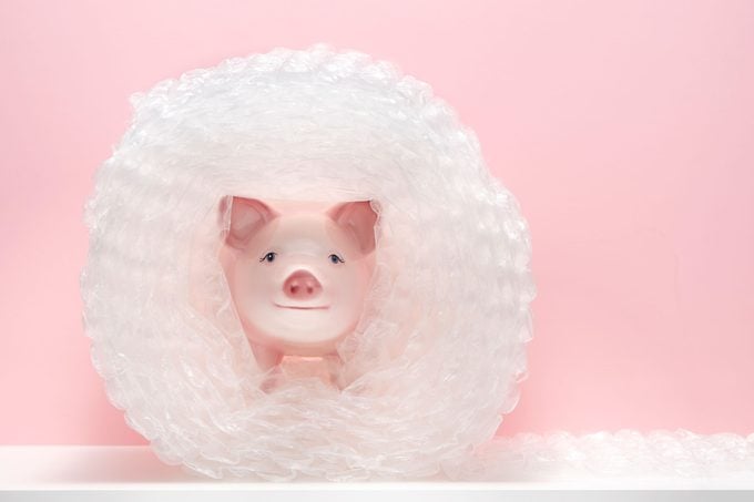 pink ceramic piggy bank wrapped in many layers of protective bubble wrap on white shelf, pink background