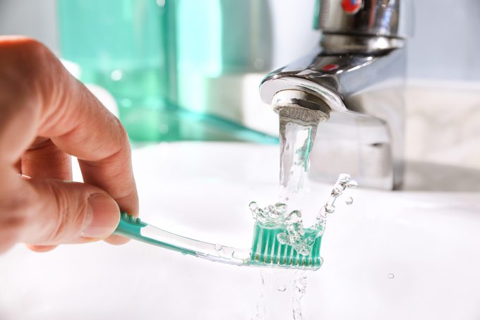 hand cleaning a toothbrush in a bathroom sink; rinsing the bristles in the stream of water