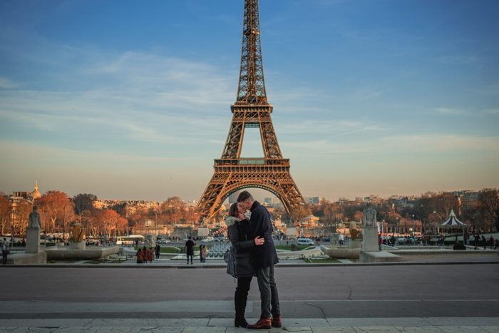 Couple Kissing While Standing On Road Against Eiffel Tower During Sunset