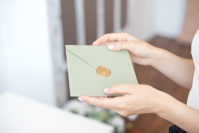 Close-up photo of female hands holding invitation envelope with a wax seal, a gift certificate, a postcard, wedding invitation card.